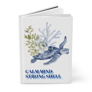 May include: A white journal featuring a watercolor design of a blue sea turtle, coral, and flowers. The text "CALM MIND STRONG SHELL" is printed in blue at the bottom. The journal is open, revealing blank pages.
