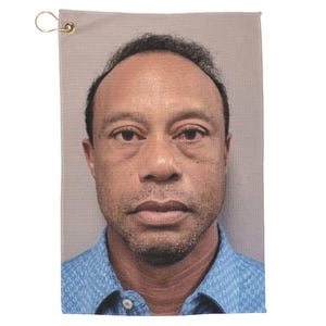 May include: A golf towel featuring a portrait of a man in a blue collared shirt. The towel is rectangular, with a brass grommet and a loop for hanging. The man has short dark hair and a neutral expression.