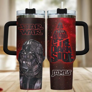 May include: Two stainless steel tumblers with black handles and lids featuring Star Wars graphics. One shows Darth Vader with the text I don't like sand, it's coarse and rough and irritating and it gets everywhere. The other features the text You don't know the power of the dark side and the name James.