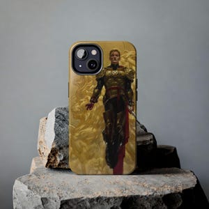 May include: A smartphone case featuring a graphic illustration of a figure in ornate gold armor with a red cape, standing against a golden background with a lion motif. The case has a cutout for the camera lens and is rectangular in shape.