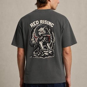 May include: Dark gray t-shirt with a graphic of a wolf holding a weapon, with the words "RED RISING" above the wolf. The wolf is black and white with red accents. The shirt is a short-sleeved crew neck.