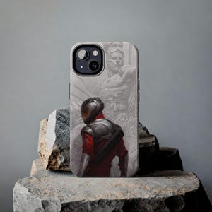 May include: A smartphone case featuring a graphic illustration of a figure in a dark helmet and red suit standing before a large, faded, monochromatic statue of a bearded warrior wearing a helmet and armor, set against a light gray background.