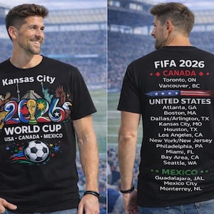 May include: Black t-shirt with "Kansas City 2026 World Cup" graphic. The front features a soccer ball and the flags of USA, Canada, and Mexico. The back lists FIFA 2026 host cities in Canada, the United States, and Mexico.
