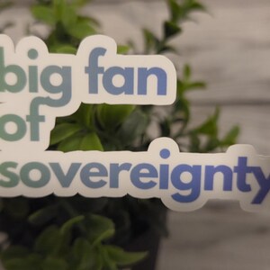 May include: A die-cut vinyl sticker featuring the text "big fan of sovereignty." in a bold, sans-serif font. The lettering transitions from a muted teal on the left to a deep blue on the right, set against a clean white background border.