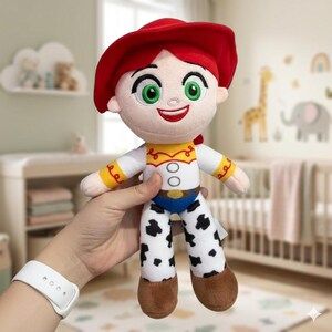 Pode incluir: Boneca de pel&uacute;cia de um personagem com chap&eacute;u vermelho, olhos verdes e boca vermelha sorrindo. A boneca usa uma camisa branca com detalhes amarelos, cinto azul e cal&ccedil;as estampadas em preto e branco. &Eacute; um brinquedo infantil.