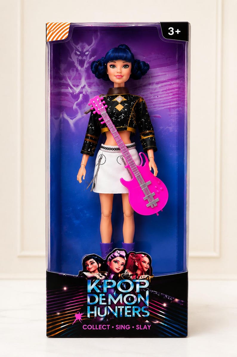 May include: A doll in a clear plastic box. The doll has blue hair, a black and gold top, a white skirt, and purple boots. She holds a pink guitar. The box reads "KPOP DEMON HUNTERS" and "COLLECT. SING. SLAY."