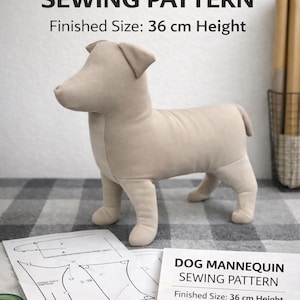 May include: A beige dog mannequin, approximately 14 inches tall, stands on a checkered surface. The image includes sewing patterns, scissors, thread, and a measuring tape. Text on the image reads "DOG MANNEQUIN SEWING PATTERN" and "Finished Size: 36 cm Height."