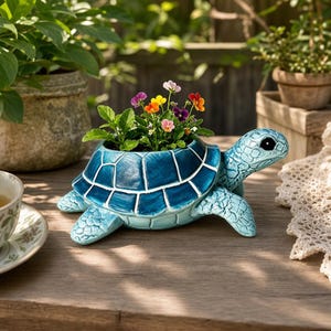 Könnte beinhalten: Blauer Keramik-Schildkröten-Blumentopf mit mosaikartigem Schalendesign. Der Topf ist mit bunten Stiefmütterchen und grünem Laub gefüllt. Die Schildkröte hat detaillierte Merkmale und steht auf einer Holzoberfläche.