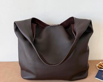 May include: A dark brown hobo bag with a pebbled texture and a wide, integrated shoulder strap. The bag features a slouchy, unstructured silhouette with a deep, open main compartment that reveals a dark brown interior lining.