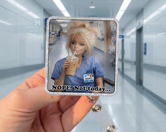 May include: A silver-framed badge reel featuring a doll-like figure in blue scrubs, drinking an iced coffee. The text "NOPE. Not today..." is displayed below the image. The reel has a clear plastic strap and a metal clip.