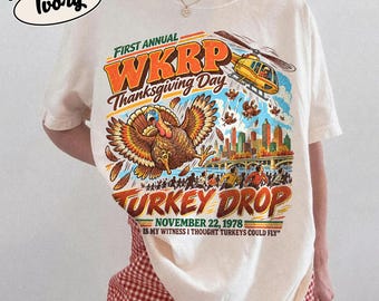May include: An ivory t-shirt featuring a graphic print of the WKRP Thanksgiving Day Turkey Drop. The design includes a yellow helicopter, a large turkey, a city skyline, and the text: First Annual WKRP Thanksgiving Day Turkey Drop November 22, 1978 IS MY WITNESS I THOUGHT TURKEYS COULD FLY.