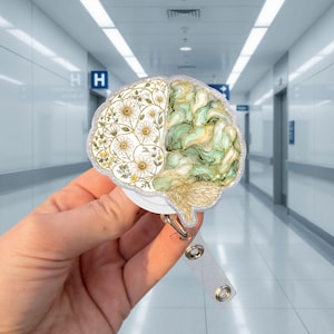 May include: A brain-shaped badge reel featuring a split design. The left side displays a detailed illustration of white daisies with yellow centres and green stems. The right side features a swirling, marbled pattern in shades of sage green and gold.