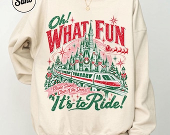 May include: A sand-colored crewneck sweatshirt featuring a graphic of a castle and a monorail train. The text reads "Oh! WHAT FUN It's to Ride!" and "Please Stand Clear of the Doors!" with red and green holiday-themed accents.
