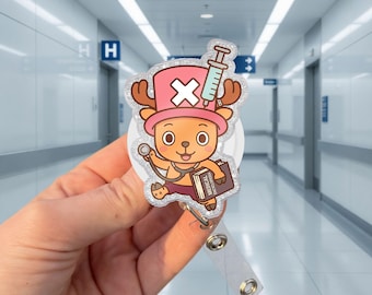 May include: A glittery acrylic badge reel featuring a cartoon reindeer character wearing a pink hat with a white X, holding a stethoscope and a book labeled Medical Encyclopedia, with a syringe graphic positioned above the character's head.