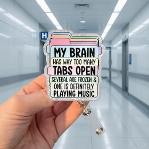 May include: A badge reel with a colorful file folder design. The text on the badge reads "MY BRAIN HAS WAY TOO MANY TABS OPEN. SEVERAL ARE FROZEN & ONE IS DEFINITELY PLAYING MUSIC."