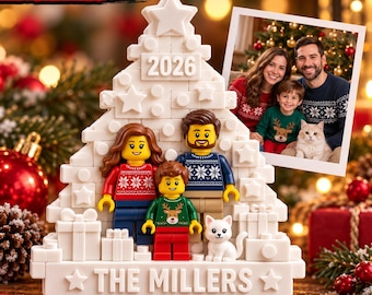 May include: A white 3D relief print Christmas tree ornament featuring three minifigures, a small cat figure, and gift boxes. The tree is topped with a star, displays the year 2026, and the text THE MILLERS at the base. A photo of a family is attached.