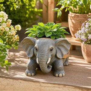 Könnte beinhalten: Grauer Elefanten-Blumentopf mit einer kleinen grünen Pflanze. Der Elefant hat große Ohren, Stoßzähne und einen Rüssel. Der Topf besteht aus einem haltbaren Material und ist für den Innen- und Außenbereich geeignet.
