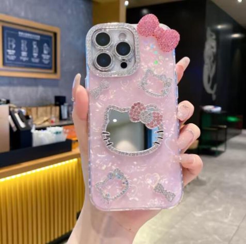 Puede incluir: Funda de tel&eacute;fono rosa con dise&ntilde;o de Hello Kitty. La funda presenta un lazo brillante, pedrer&iacute;a y una cara de Hello Kitty espejada. La funda tiene un acabado brillante e iridiscente y est&aacute; dise&ntilde;ada para un tel&eacute;fono inteligente.