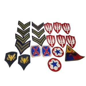 May include: A collection of military patches and insignia, including chevrons, shield-shaped patches with white wings, and patches with crossed swords. Also included are patches with a blue star on a red background and patches with a yellow eagle.