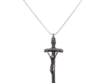 Puede incluir: Un collar con colgante plateado que presenta un crucifijo detallado. La cruz representa la figura de Jesucristo y está suspendida de una delicada cadena plateada. El fondo es blanco.