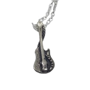 May include: A silver-toned metal pendant shaped like an electric guitar, featuring detailed textured lines and a smooth neck, suspended from a matching silver-toned metal link chain. The pendant has a dark, oxidized finish in the recessed areas.