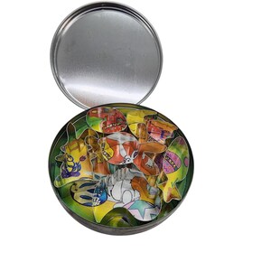 May include: A round, silver tin with a lid, open to reveal colorful Easter-themed cookie cutters. The cutters include bunnies, eggs, and other festive shapes. The tin is on a white background.