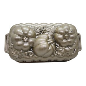 May include: A rectangular metallic gold-toned baking pan featuring a molded design of three pumpkins surrounded by leaves and vines. The brand name Nordic Ware is embossed on the side handles of this cast aluminum kitchen bakeware item.