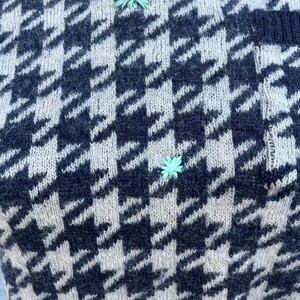 Puede incluir: Primer plano de un su&eacute;ter de punto con un cl&aacute;sico estampado de pata de gallo en azul marino y blanco roto. El su&eacute;ter presenta peque&ntilde;os detalles florales bordados en azul claro. La tela parece suave y texturizada, con puntadas de punto visibles.