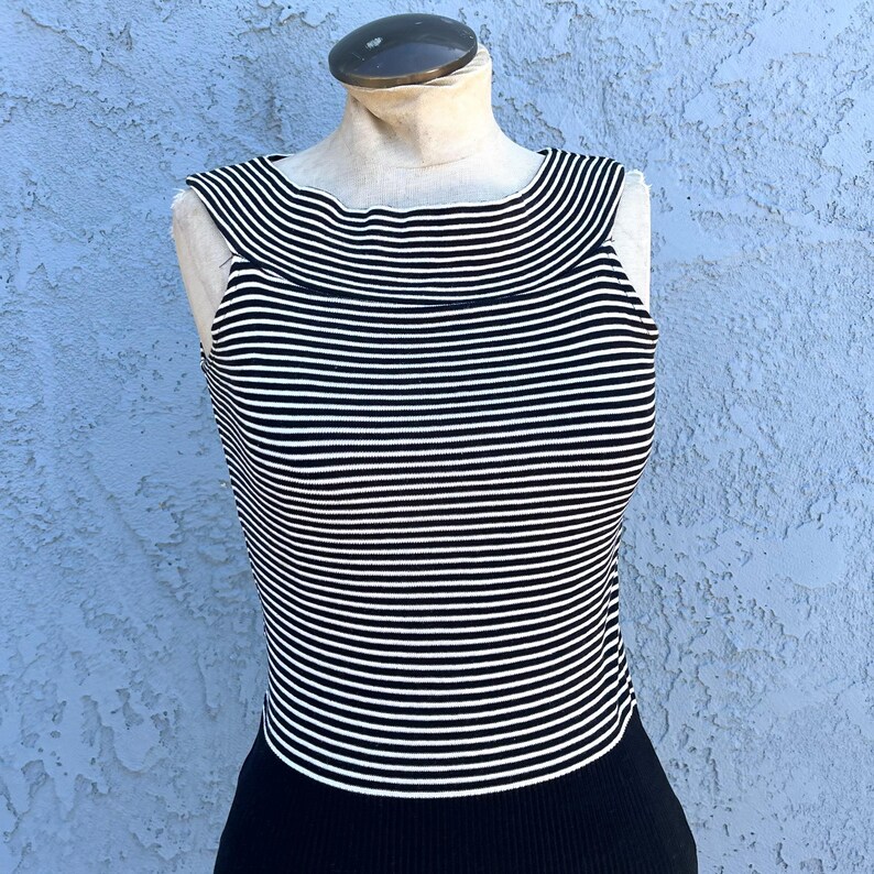 May include: A sleeveless top with horizontal black and white stripes. The top has a scoop neckline and is displayed on a mannequin. The bottom portion of the top is solid black.