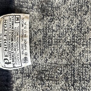 Puede incluir: Primer plano de un su&eacute;ter de punto gris y blanco con una etiqueta que dice "Pendleton" y "100% lana virgen". La etiqueta tambi&eacute;n indica que el su&eacute;ter es talla M y est&aacute; hecho en los EE. UU.