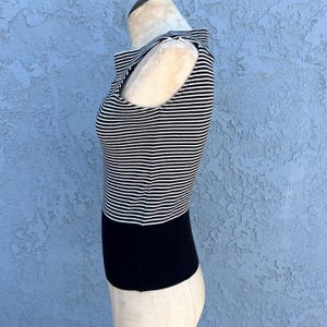 May include: A sleeveless top with horizontal black and white stripes on the upper portion and a solid black lower section. The top has a high neckline and is displayed on a mannequin.