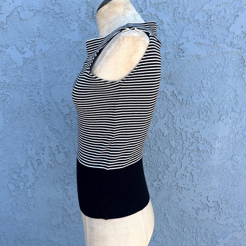 May include: A sleeveless top with horizontal black and white stripes on the upper portion and a solid black lower section. The top has a high neckline and is displayed on a mannequin.