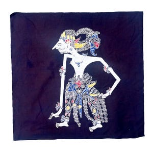 Op de afbeelding: Een witte schaduwpop op een donkerblauwe achtergrond. De pop is een gestileerde figuur met een groot hoofd en lange ledematen. De pop draagt een kleurrijk kostuum met ingewikkelde details.