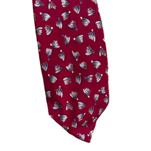 May include: A red necktie with a repeating pattern of white and gray abstract shapes. The tie is made of a smooth fabric and has a classic pointed end. The design is a mix of modern and classic styles.