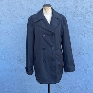 May include: A black double-breasted coat with a notched collar and six black buttons. The coat has long sleeves and a classic, tailored design. The coat is displayed on a mannequin against a blue background.