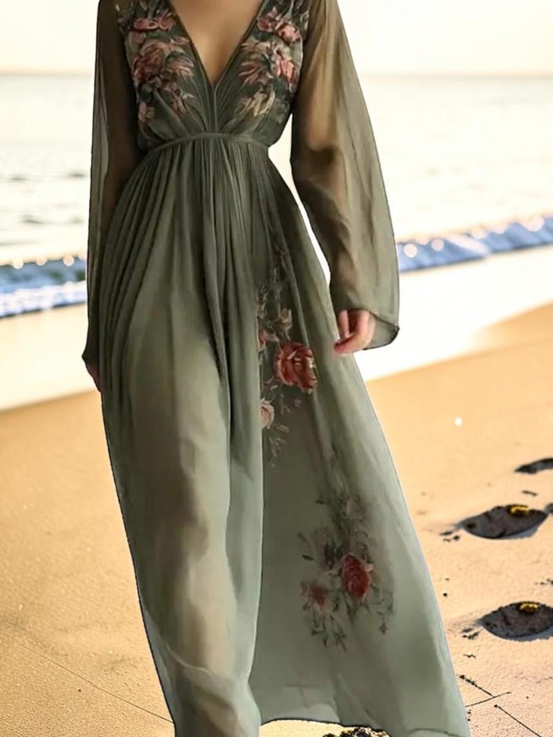 May include: A flowing, olive green maxi dress with long sleeves and a deep V-neck. The dress features floral embroidery on the bodice and skirt. The sheer fabric creates a light and airy look, perfect for a beach setting.