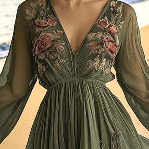 May include: Olive green chiffon dress with a deep V-neckline and long, flowing sleeves. The bodice and sleeves are adorned with embroidered floral details in shades of pink and red. The dress has a gathered waist and a flowing skirt.