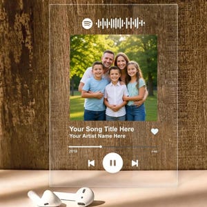 May include: A transparent acrylic plaque with a family photograph, Spotify logo, and music player design. The text reads "Your Song Title Here" and "Your Artist Name Here". White wireless earbuds are in the foreground.