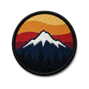 May include: Round embroidered patch featuring a mountain scene. The design includes a snow-capped mountain peak, dark blue trees, and a sunset gradient of orange, red, and yellow. The patch has a black border.