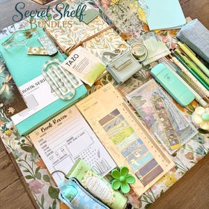 May include: A collection of stationery items, such as notebooks, pens, and sticky notes, arranged on a floral fabric. Includes a decorative jar and a small purse. The text "Secret Shelf Bundles" is visible.