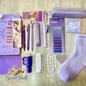 May include: A selection of purple stationery and accessories, including a notebook, pens, a pencil case, sticky notes, and a fluffy sock. The items are arranged on a light surface. The notebook has a sun and moon design.