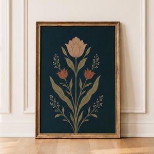 May include: A framed botanical print featuring a stylized floral design. The artwork showcases a central flower with peach-colored petals, flanked by smaller red flowers and green foliage against a dark blue background. The frame is a warm, natural wood tone.