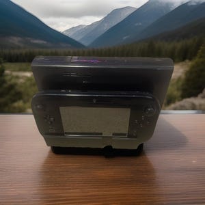 Puede incluir: Una consola Nintendo Wii U negra y una base de carga se muestran sobre una superficie de madera. La consola está en primer plano, con la base detrás. El fondo presenta una vista panorámica de montañas y árboles.