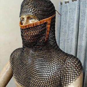May include: A black chainmail coif featuring a tan leather face mask integrated into the metal rings. The hood covers the head and shoulders, constructed from interlocking dark metal links, with a leather strap securing the nose and mouth area.