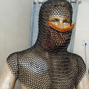 May include: A black chainmail coif featuring interlocking metal rings that cover the head, neck, and shoulders. The headpiece includes a horizontal tan leather strap across the nose area, leaving the eyes exposed while covering the lower face.
