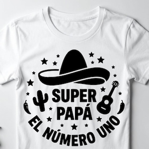 May include: A white t-shirt featuring a black graphic print of a sombrero, a cactus, a guitar, and two chili peppers. The text reads "SUPER PAPÁ EL NÚMERO UNO" in a bold, black font, surrounded by small star shapes arranged in a circular pattern.