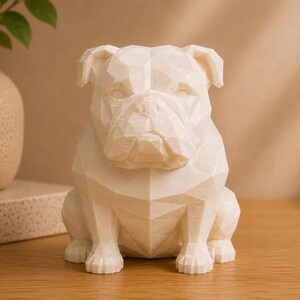May include: A cream-colored, low-poly geometric bulldog figurine featuring a faceted, angular surface design. The sculpture is rendered in a solid, matte material and depicts the dog in a seated, forward-facing position with distinct ears.