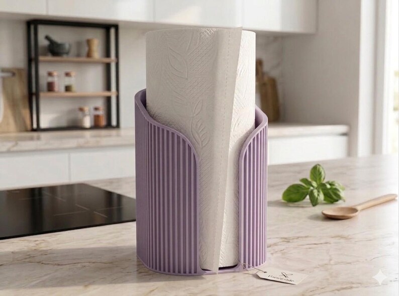 May include: A cylindrical lavender paper towel holder with a vertical ribbed texture, containing a roll of white paper towels embossed with a leaf pattern. A small rectangular tag is attached to the base of the holder.