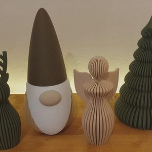 May include: A set of four decorative figures including a dark green reindeer, a gnome with a tall brown hat and white beard, a light pink angel with wings, and a dark green ribbed Christmas tree, all standing in a row.