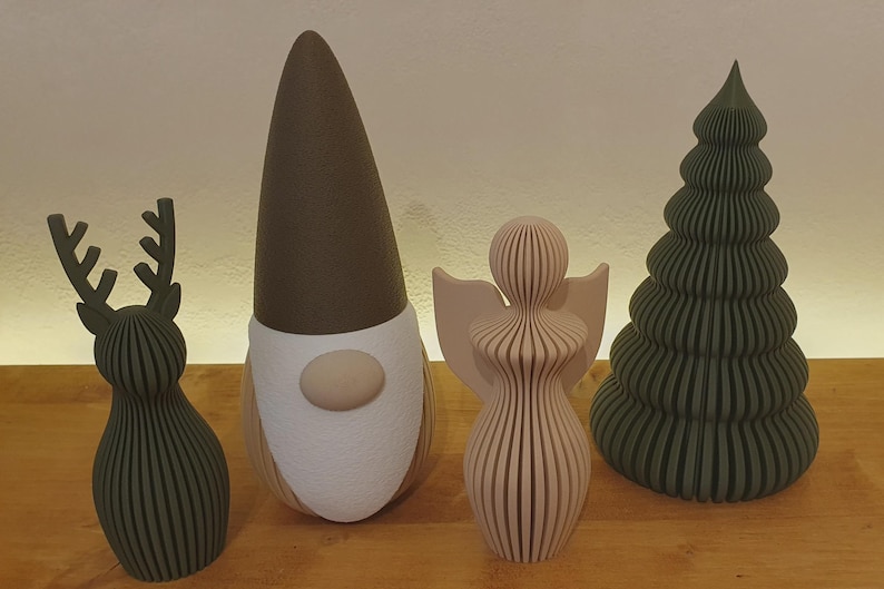 May include: A set of four decorative figures including a dark green reindeer, a gnome with a tall brown hat and white beard, a light pink angel with wings, and a dark green ribbed Christmas tree, all standing in a row.